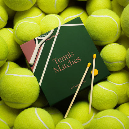 Tennis Matches box styled on a bed of neon yellow tennis balls with two long safety matches resting on top.