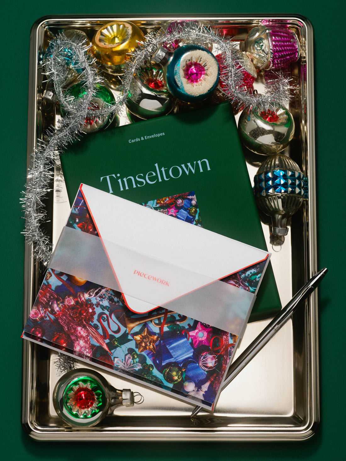 Piecework Tinseltown boxed notecard set in green with an ornament photo card and envelope on a silver tray with tinsel