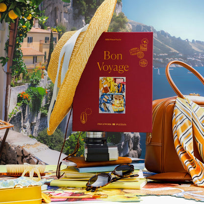 Bon Voyage puzzle box standing upright in a sunny coastal travel scene with a straw hat, leather bag, striped scarf, sunglasses, camera, and bright vacation styling.