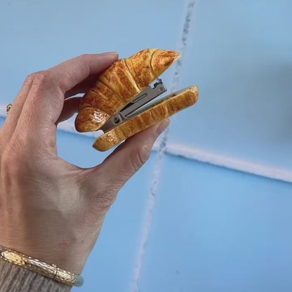 Hand-painted porcelain croissant stapler (a stapler that looks like a croissant) glistens while being rotated and squeezed while in a hand.