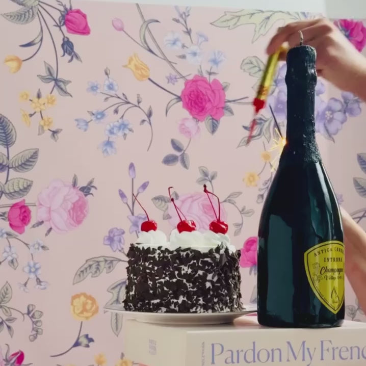 A video featuring a champagne bottle candle next to a mini cake on a box to highlight scale.