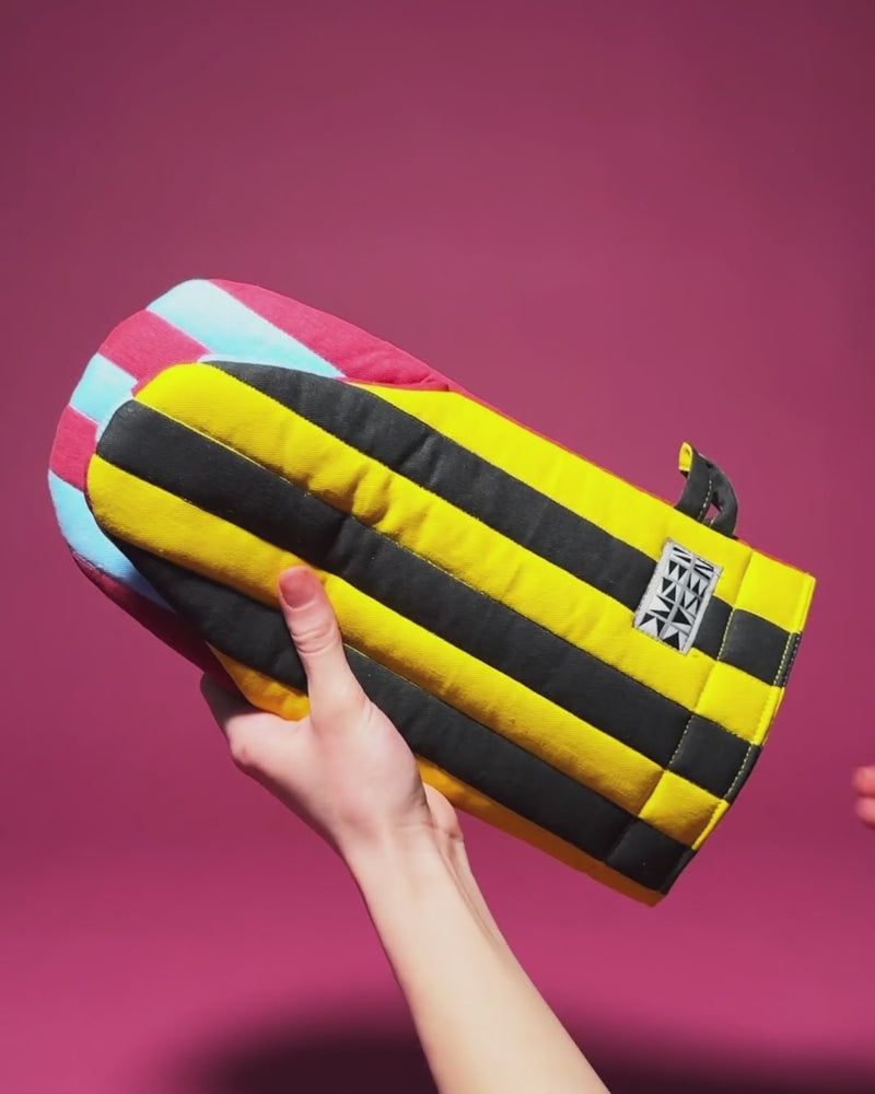 A striped oven mitt in pink, light blue, yellow, and black held up against a magenta background.