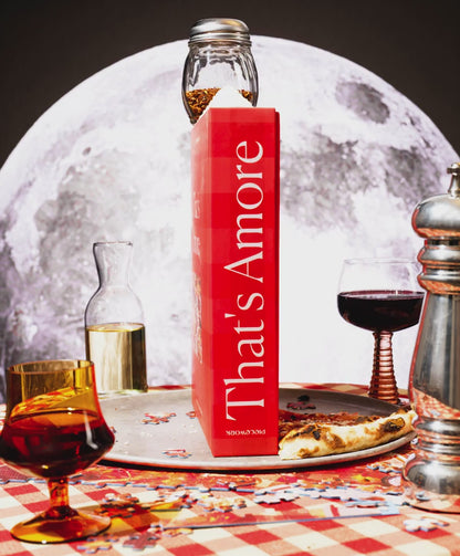 A video of the That's Amore, a 1000-piece pizza jigsaw puzzle, puzzle box rotating on a lazy susan in a red-checkered table cloth tablescape scene with the moon in the background. 
