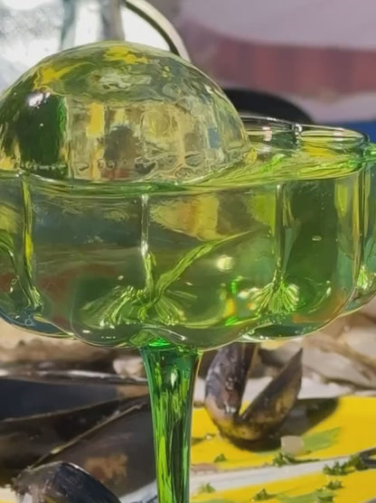 A closer look at the green Flower Champagne Coupe where the glass is filled with decorative ice and a liquid.