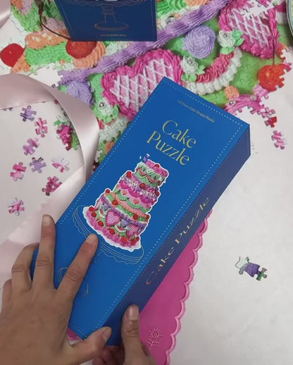 A video featuring Piecework Puzzles' Cake Puzzle, a 750-piece cake-shaped puzzle. The puzzle packaging, pieces and edges are highlighted.