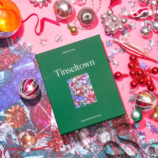 Green Tinseltown 1000-piece puzzle box on pink with silver, red and gold vintage ornaments and loose puzzle pieces